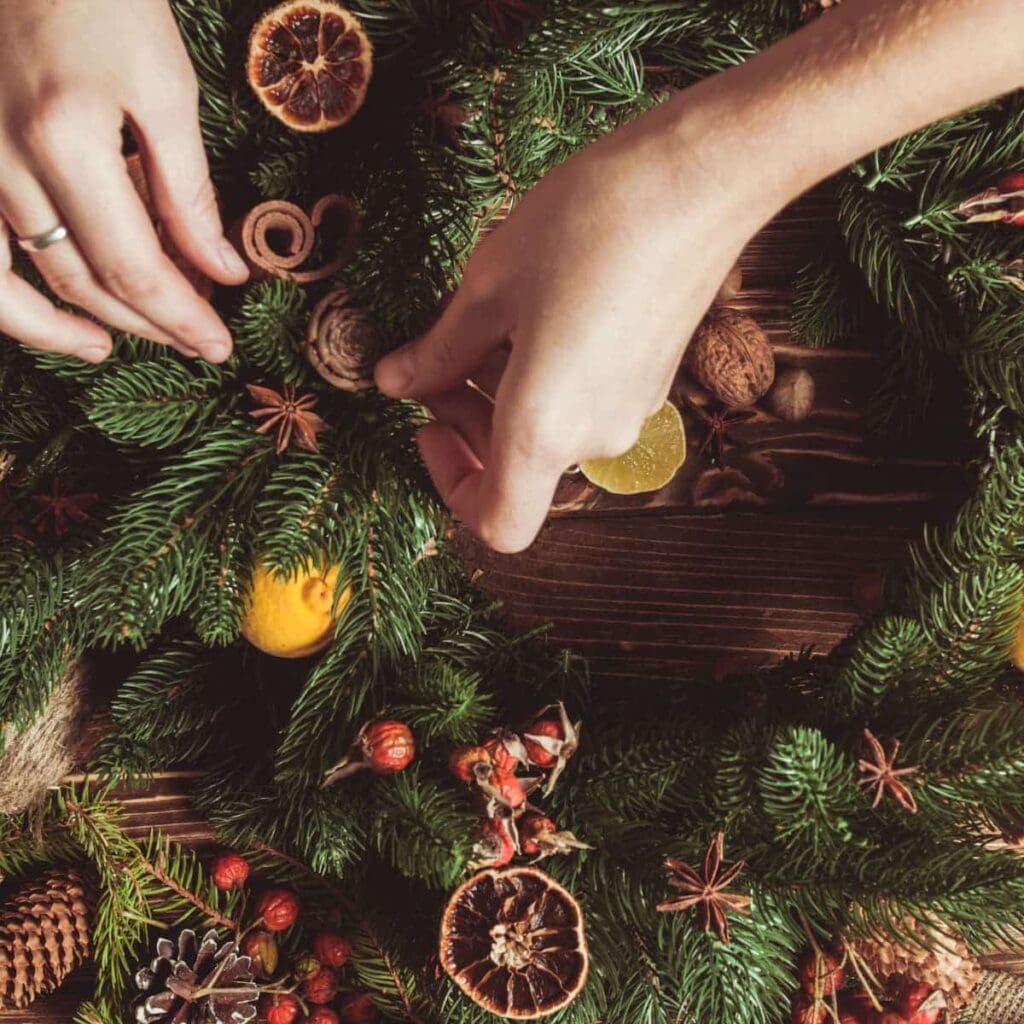 Hands decorating a festive evergreen wreath.